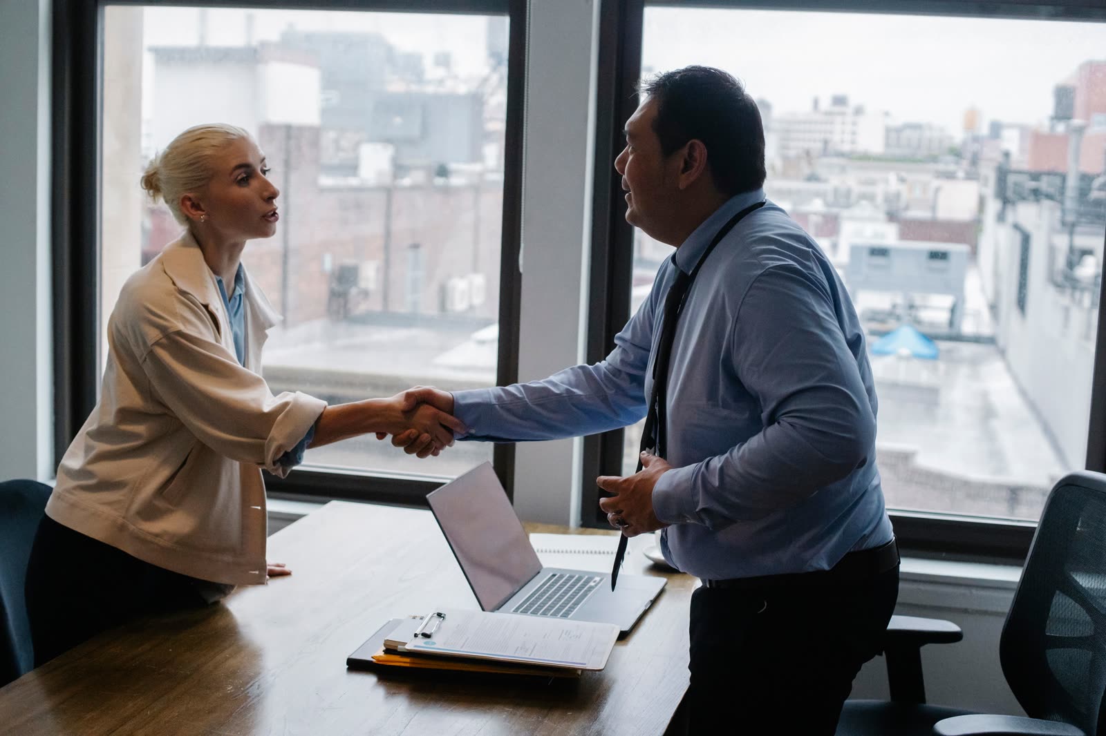 Two professionals shaking hands over a desk in an office